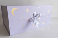 Purple gift box with star and moon designs and a silver bow on a light gray background
