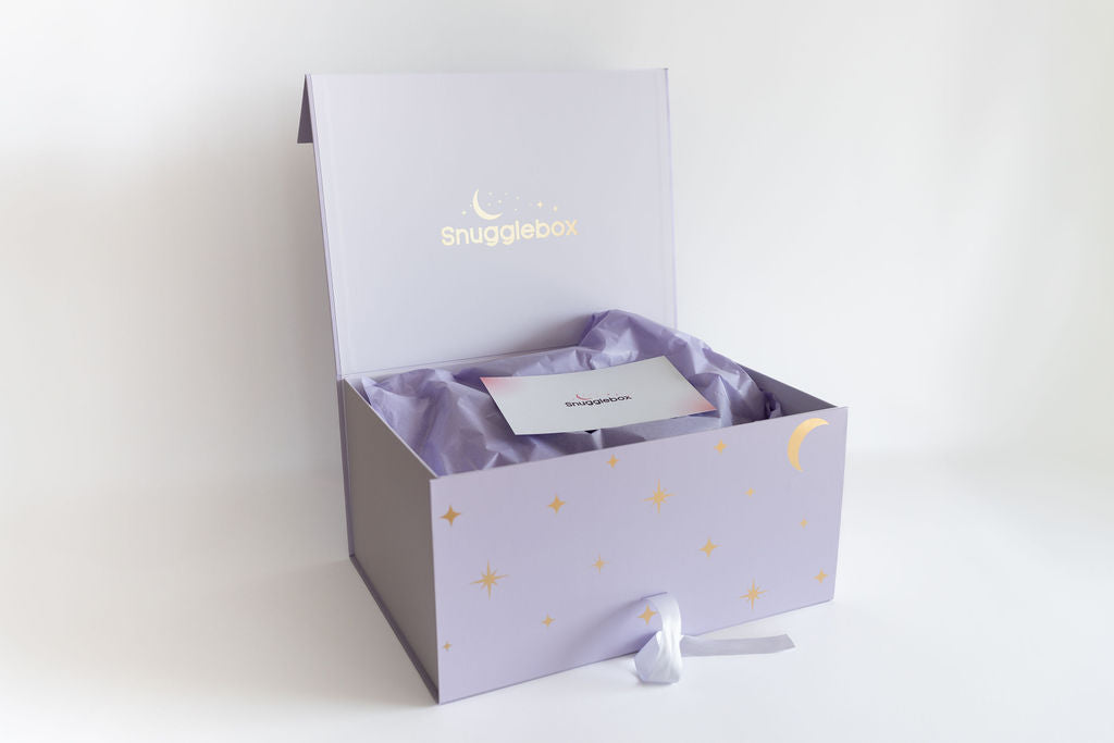 Open purple SnuggleBox with gold moon and stars, revealing soft tissue paper and a product information card, representing a delightful unboxing experience.