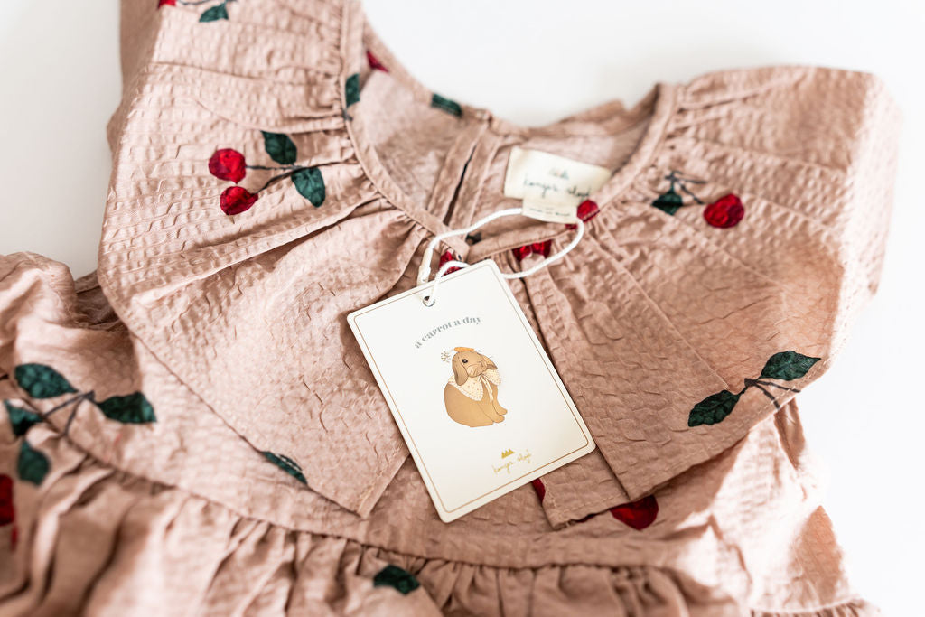 Pink children's outfit with floral embroidery and a tag on a white background