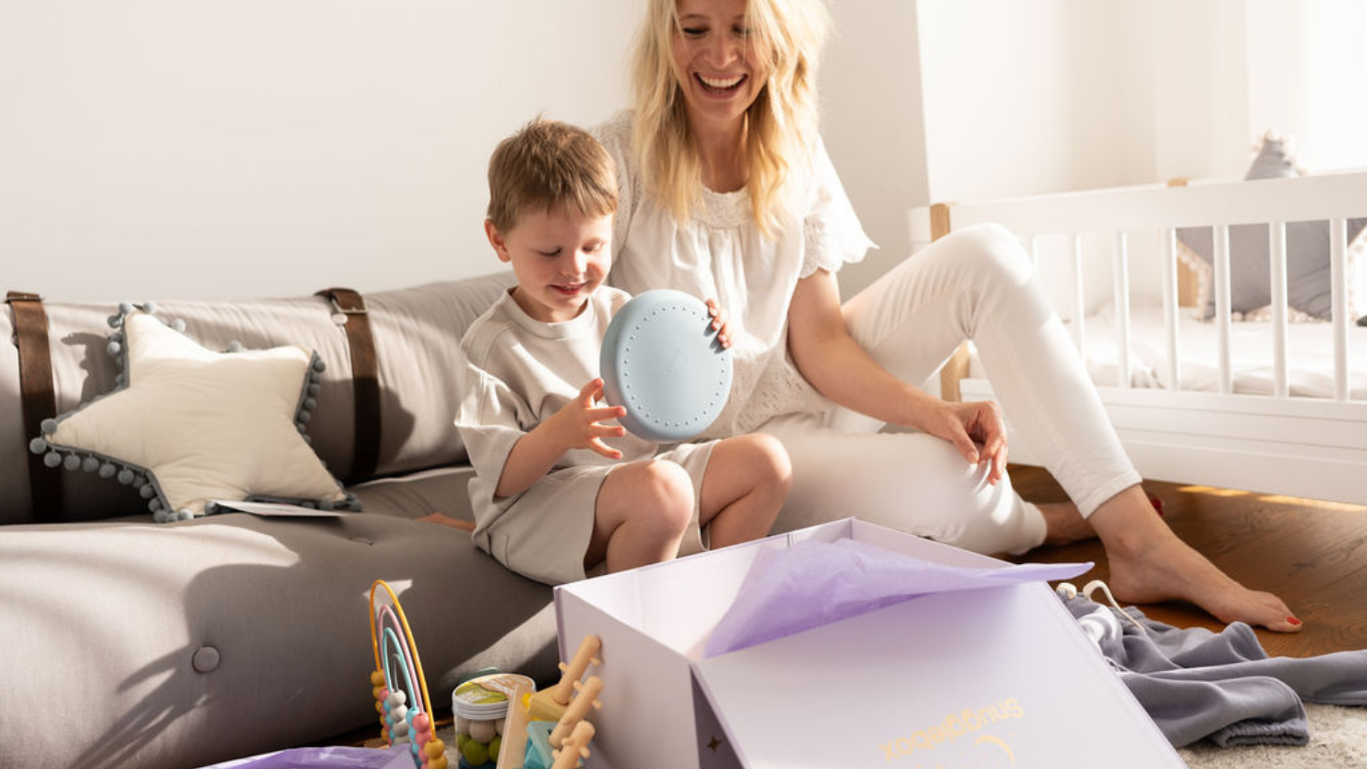 Video laden: Happy mother and child unboxing a Snugglebox, revealing exciting new toys and clothing for kids.